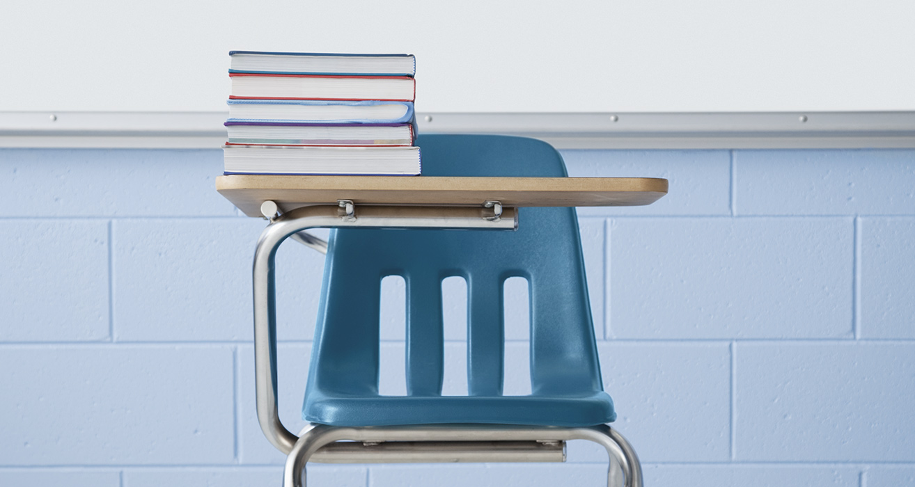 A stack of books sits on a student’s desk. 